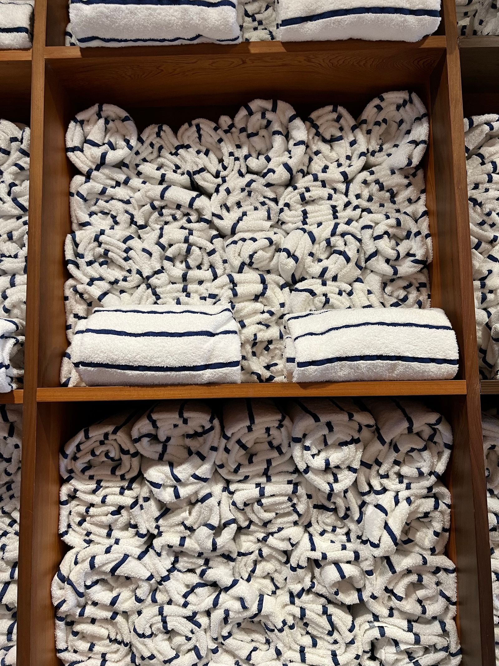 Rolled white towels with navy stripes neatly organized on wooden shelves