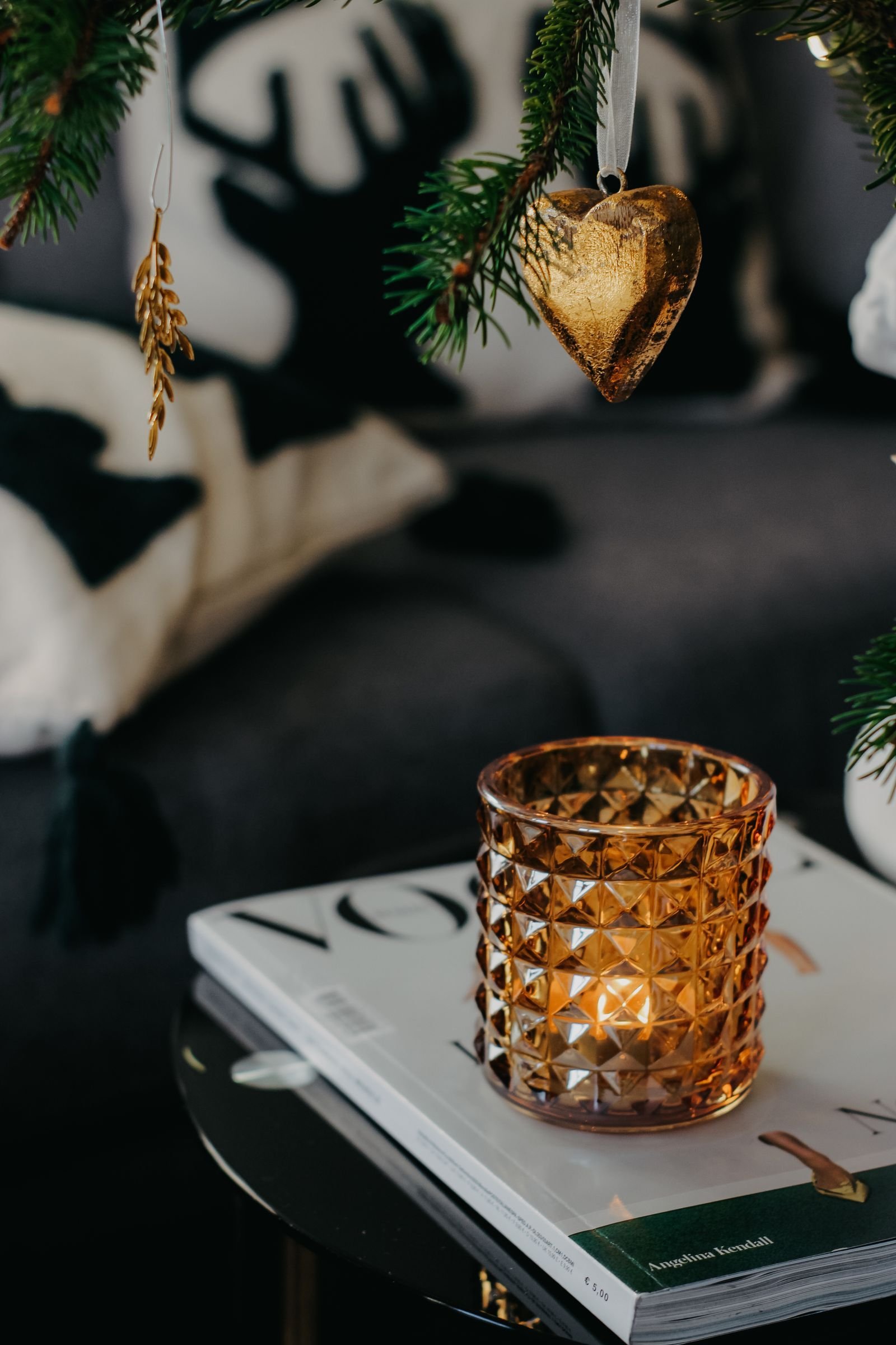 An amber glass candle holder on a stack of books on a coffee table with Christmas greenery above