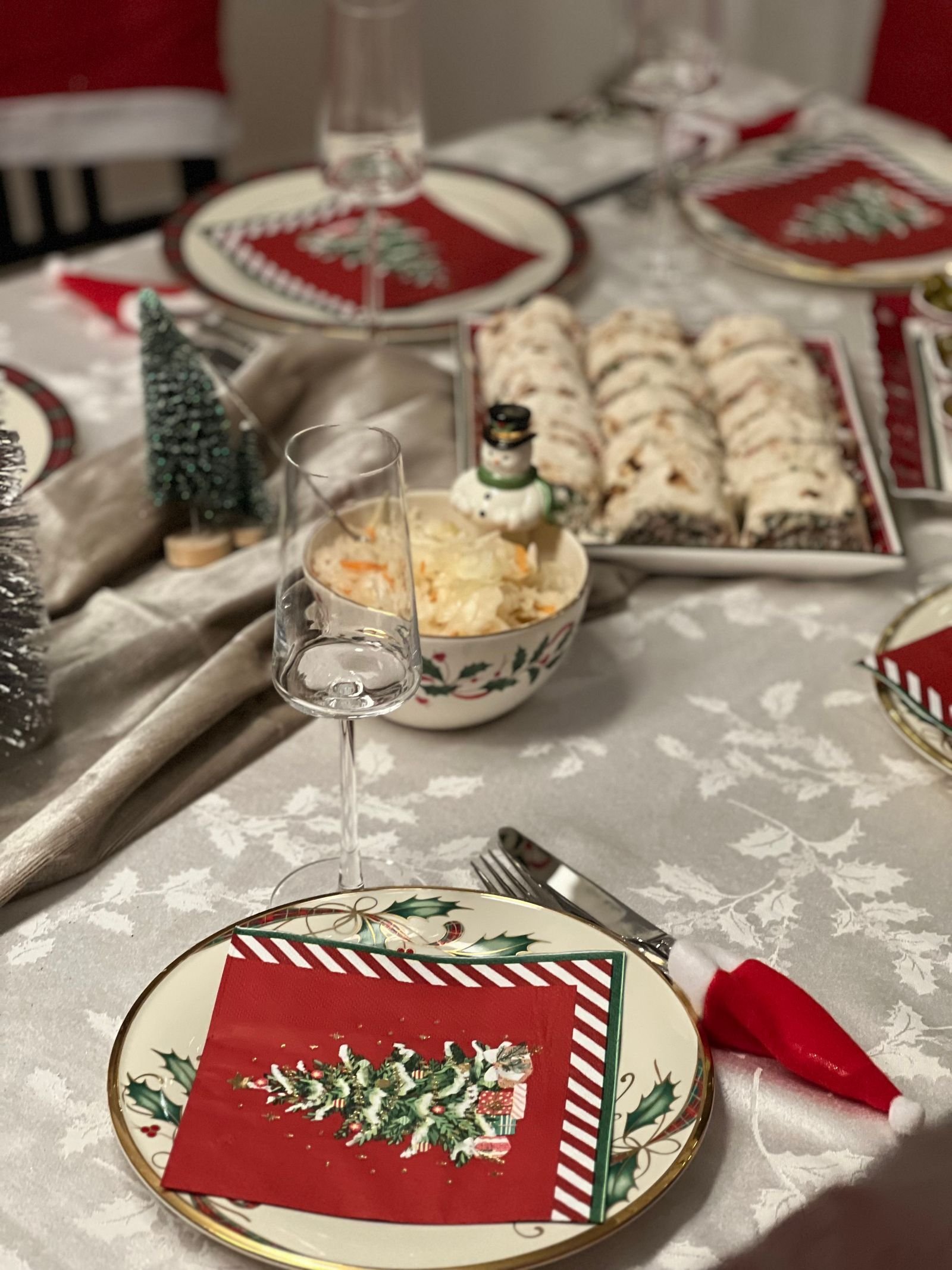 A Christmas dinner table with red napkins, festive plates, glasses and holiday treats