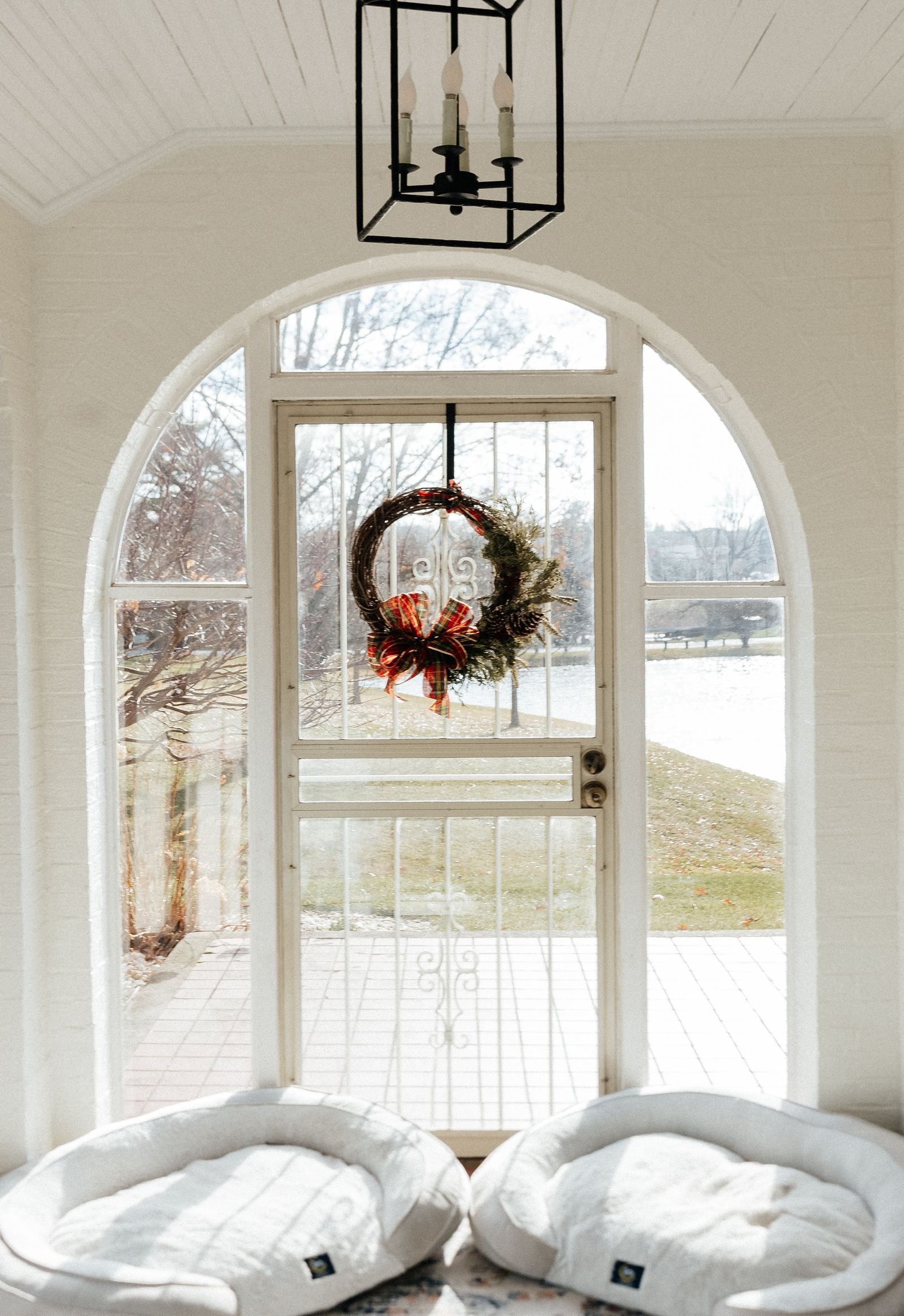 A bright entryway with a red-bowed Christmas wreath hung on an arched glass door