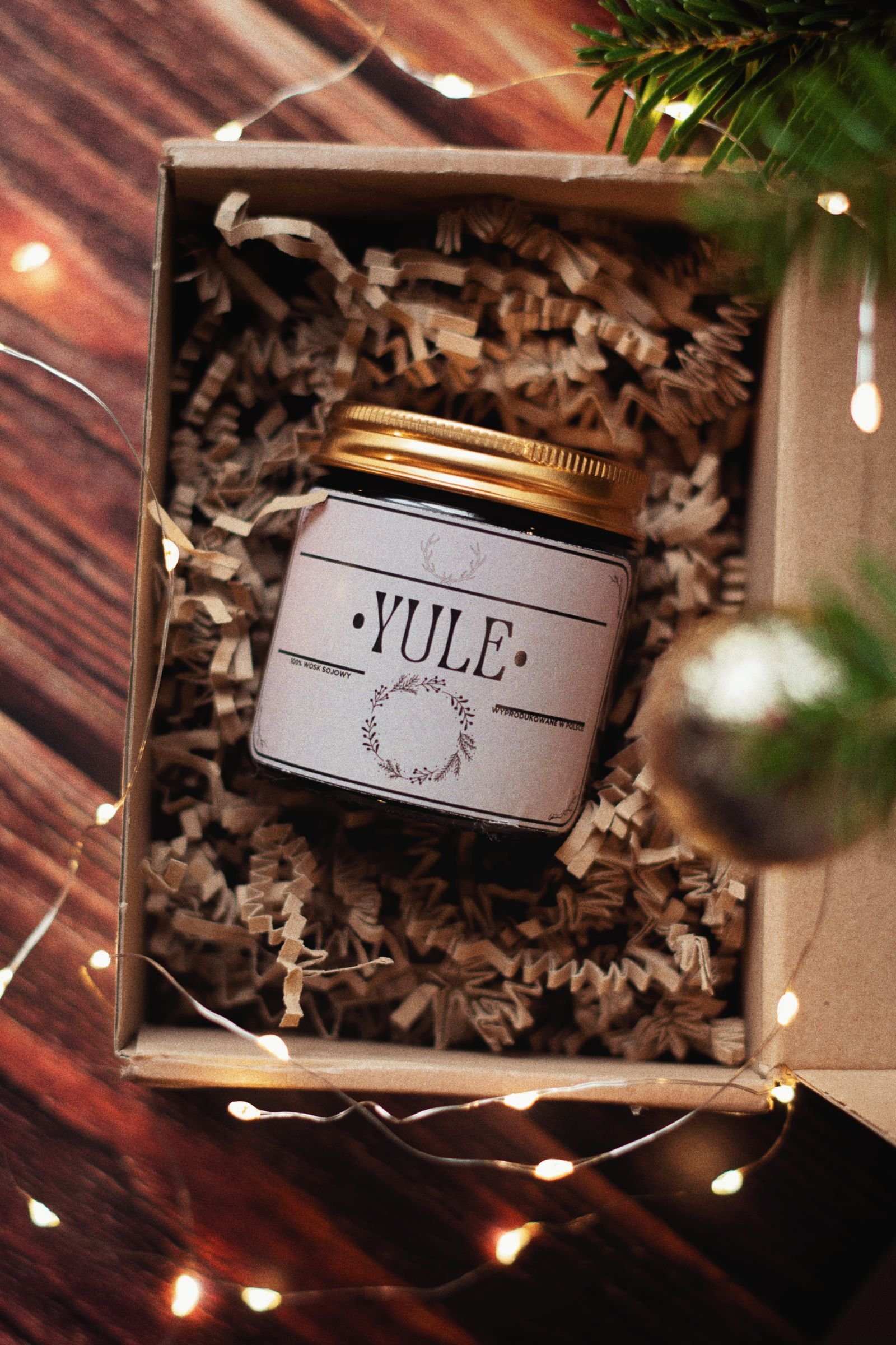 A kraft gift box with a Yule candle jar, wood shavings and warm string lights