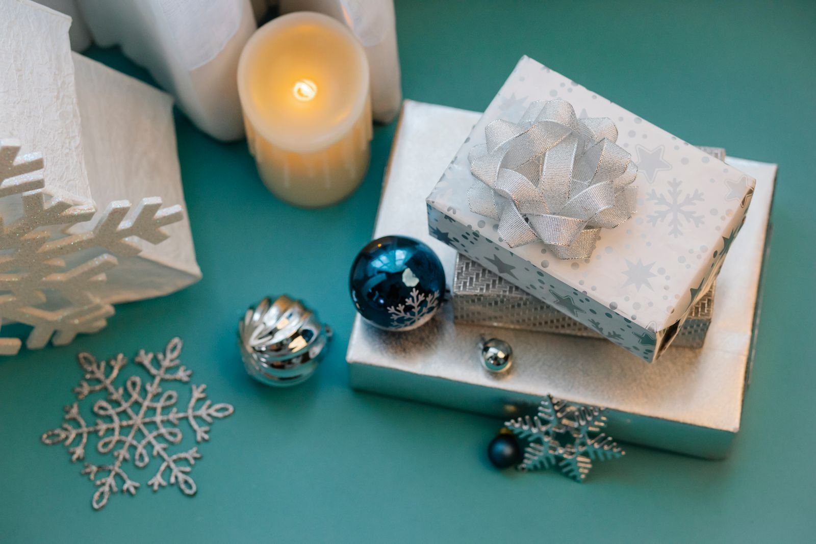 Wrapped Christmas gift boxes, a candle, ornaments and snowflake decorations on a teal table
