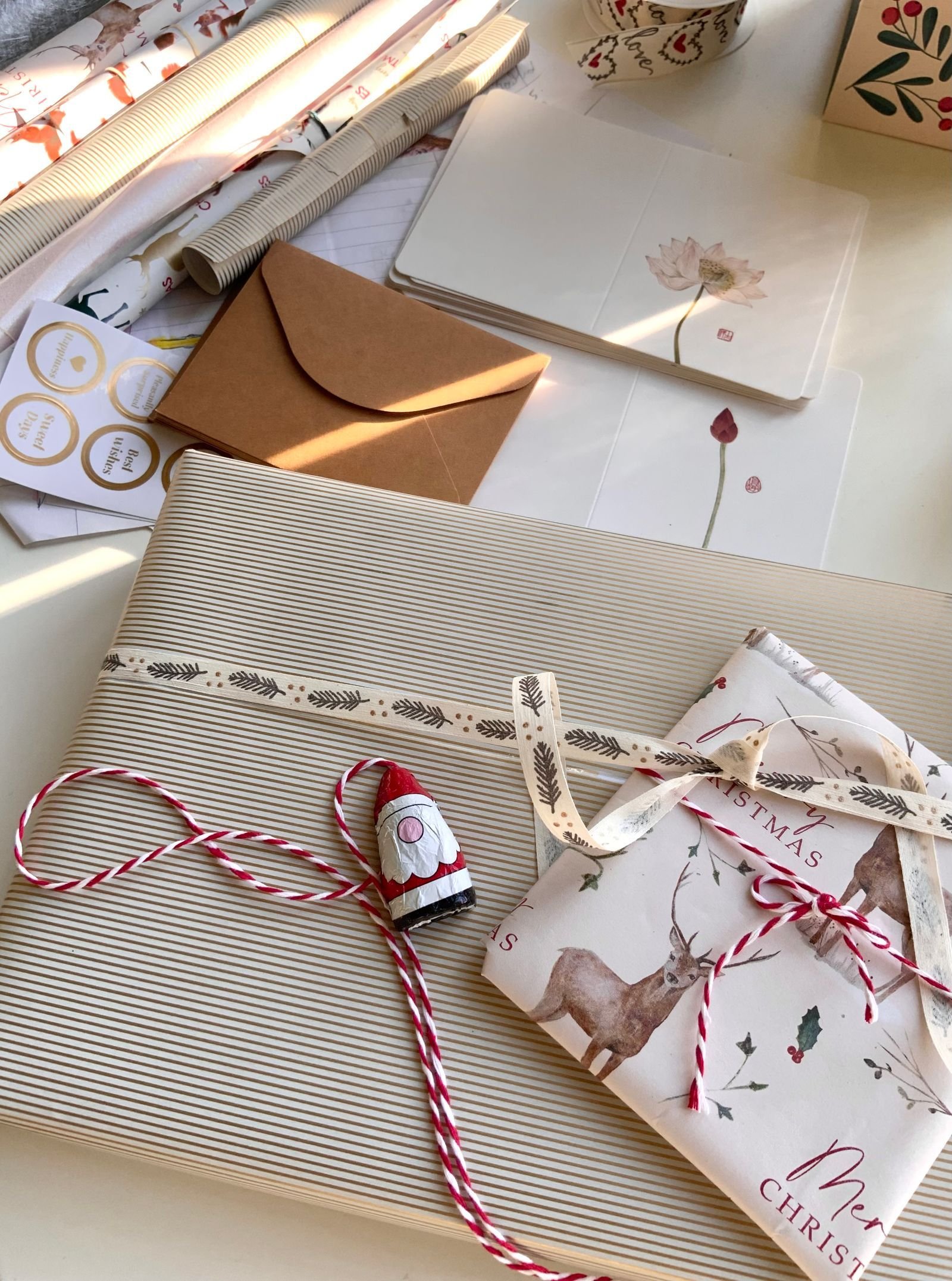 Christmas gifts wrapped in striped and deer-print paper with ribbon and red-and-white twine in sunlight