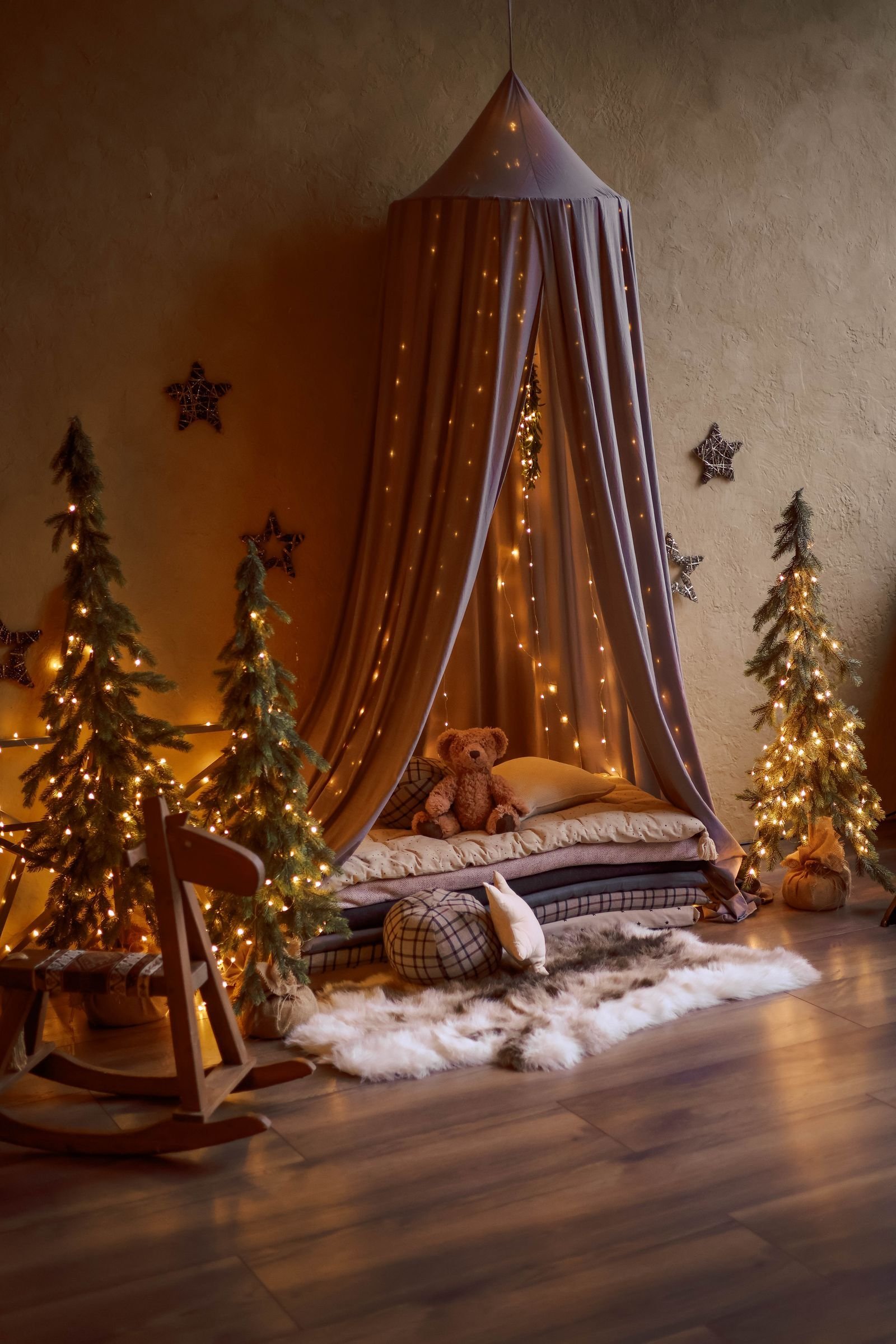 A children's bedroom with a canopy over a small bed, mini Christmas trees, star garland and warm string lights