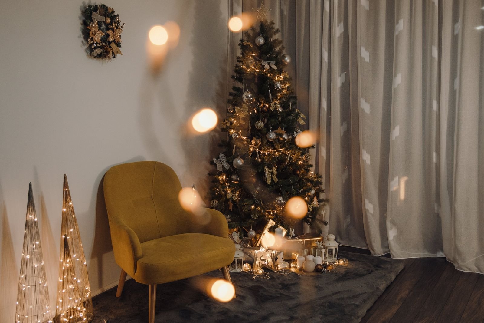A cozy corner with a mustard velvet armchair, a lit Christmas tree, a wreath and glowing light-up cone trees