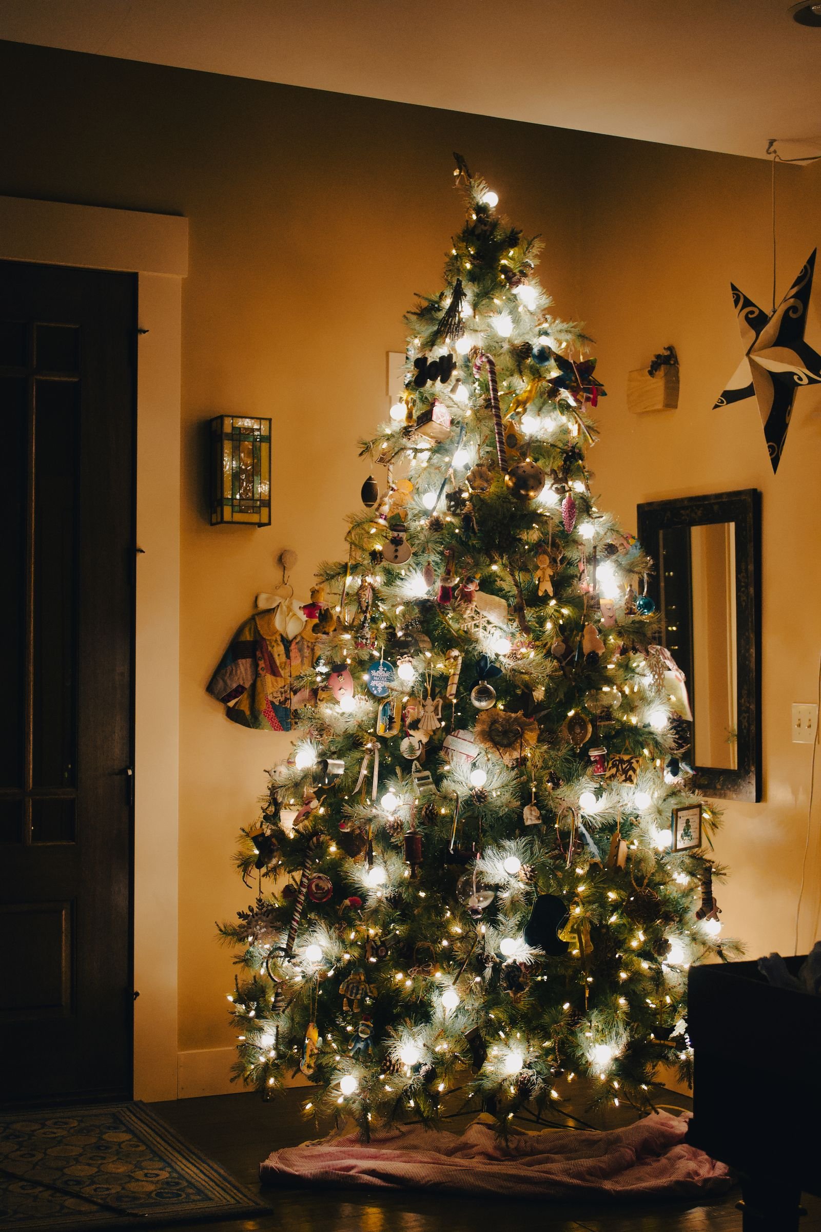 A tall Christmas tree glowing with warm white lights and ornaments in a cozy living room