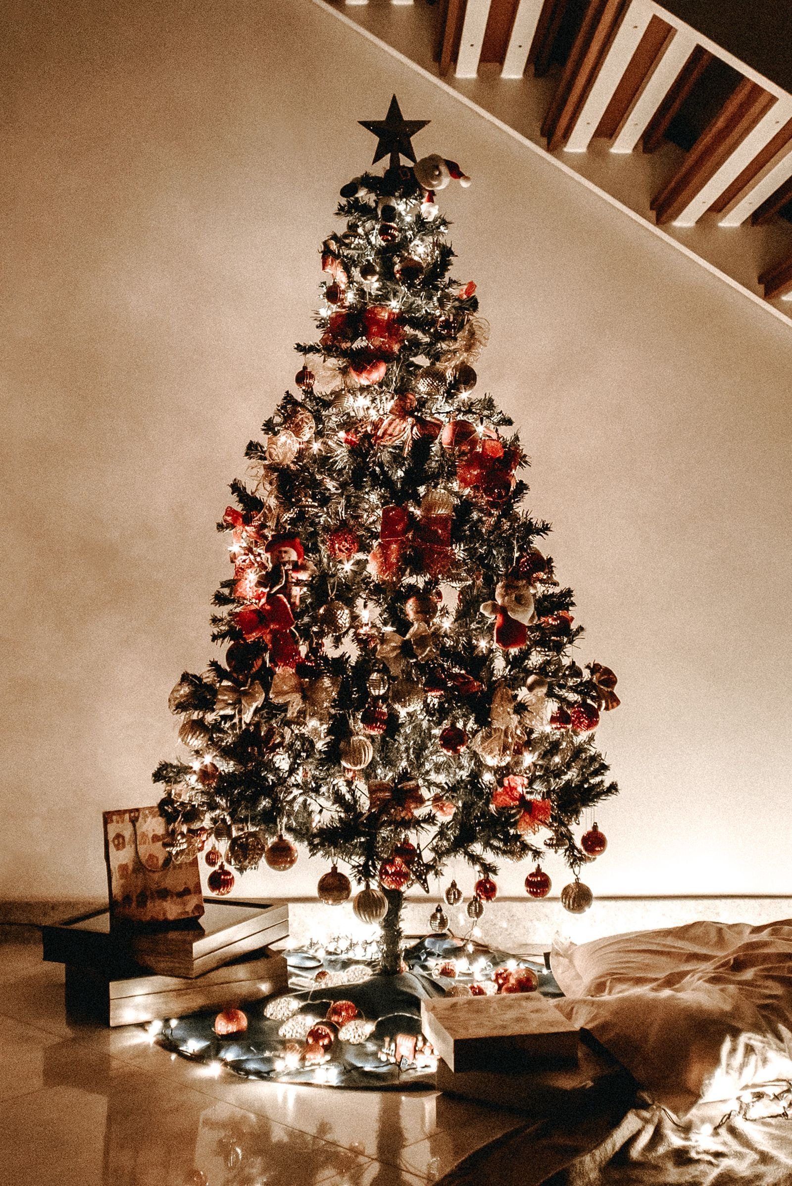 A decorated Christmas tree glowing with lights beneath a staircase, surrounded by gifts