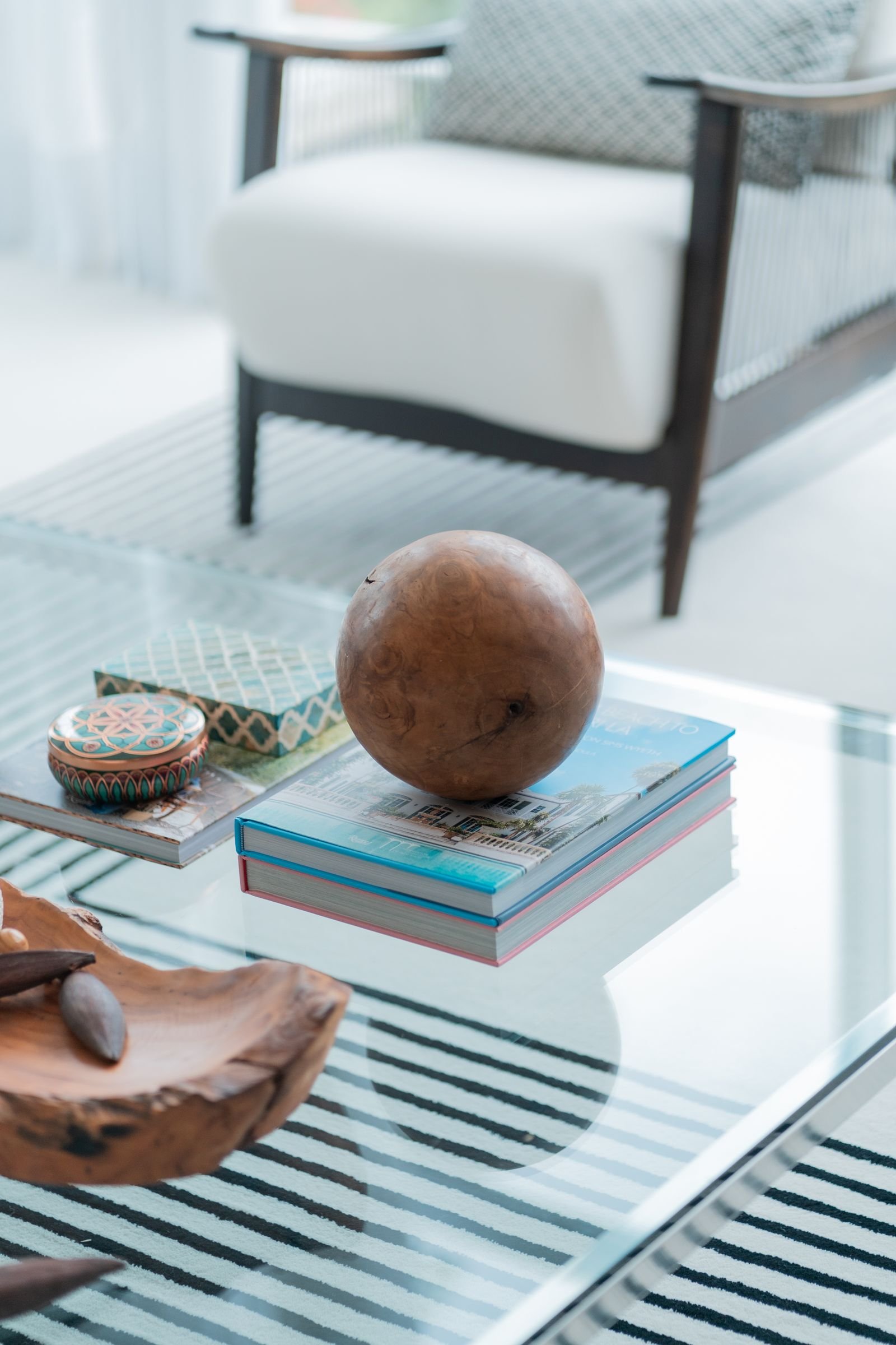 A glass coffee table styled with a stack of books, a wooden bowl and a round decorative object