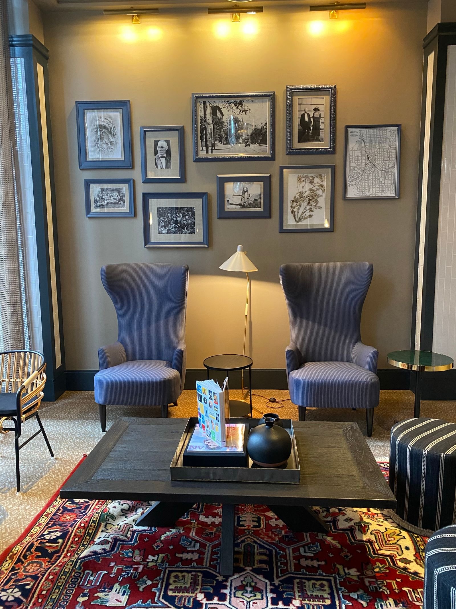 A living room gallery wall of framed photos above two blue armchairs and a coffee table