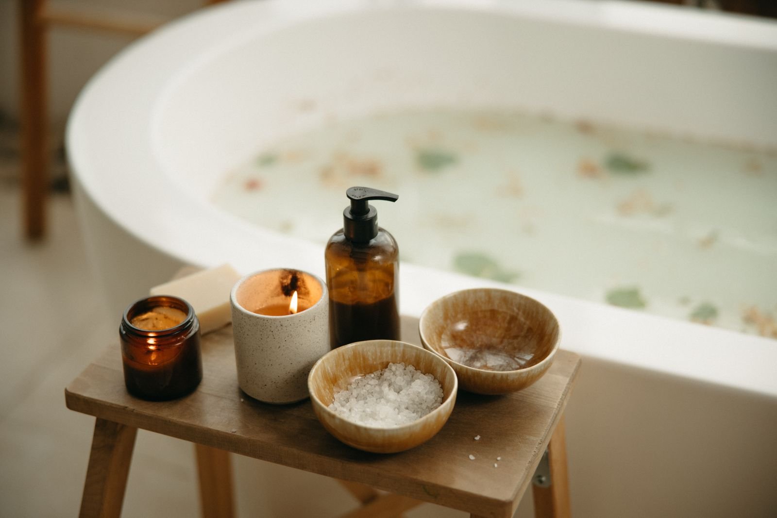 A bathtub with a wooden stool holding candles, bath salts and a soap pump