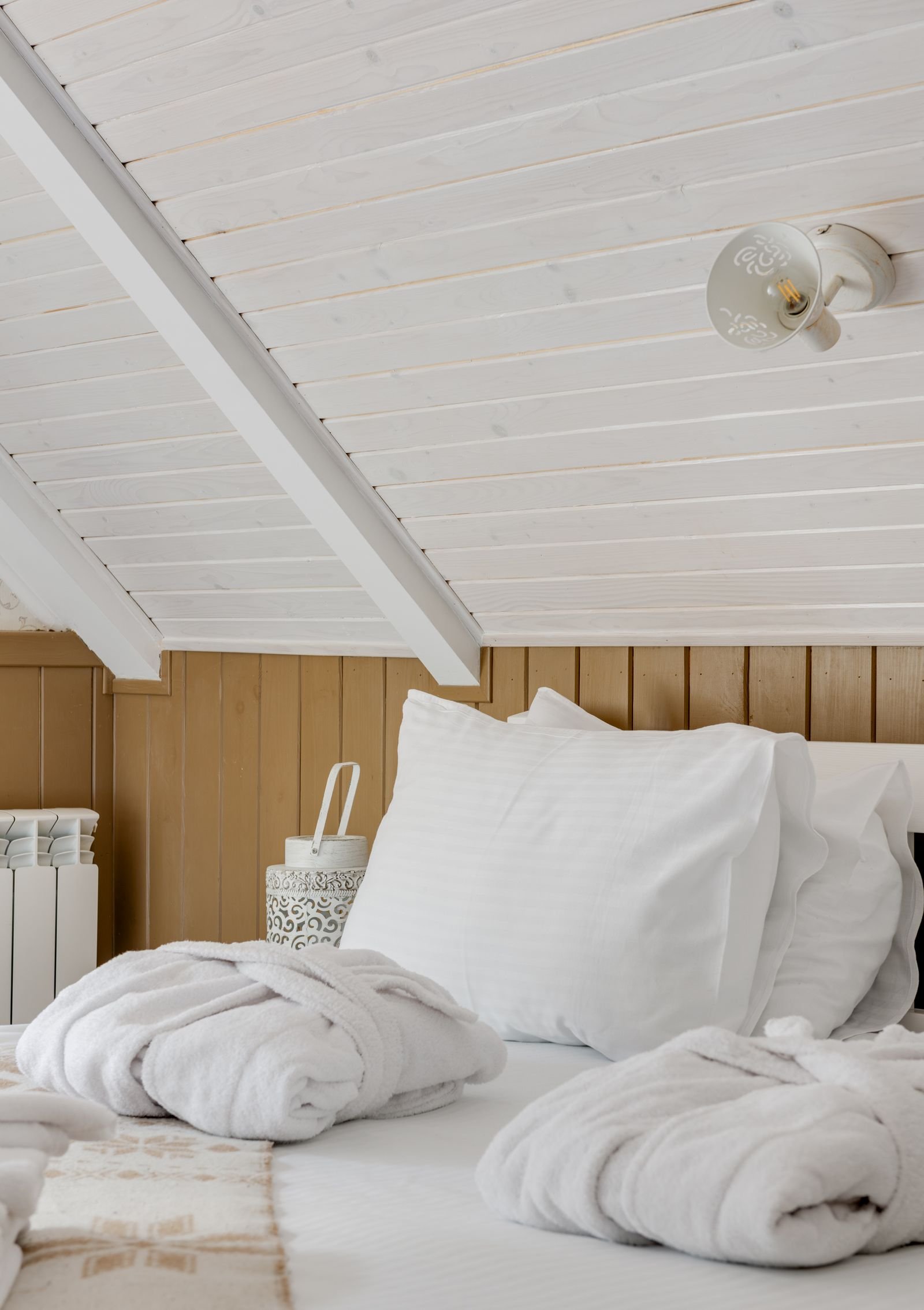 A bright attic bedroom with crisp white bedding, fluffy pillows and folded white robes