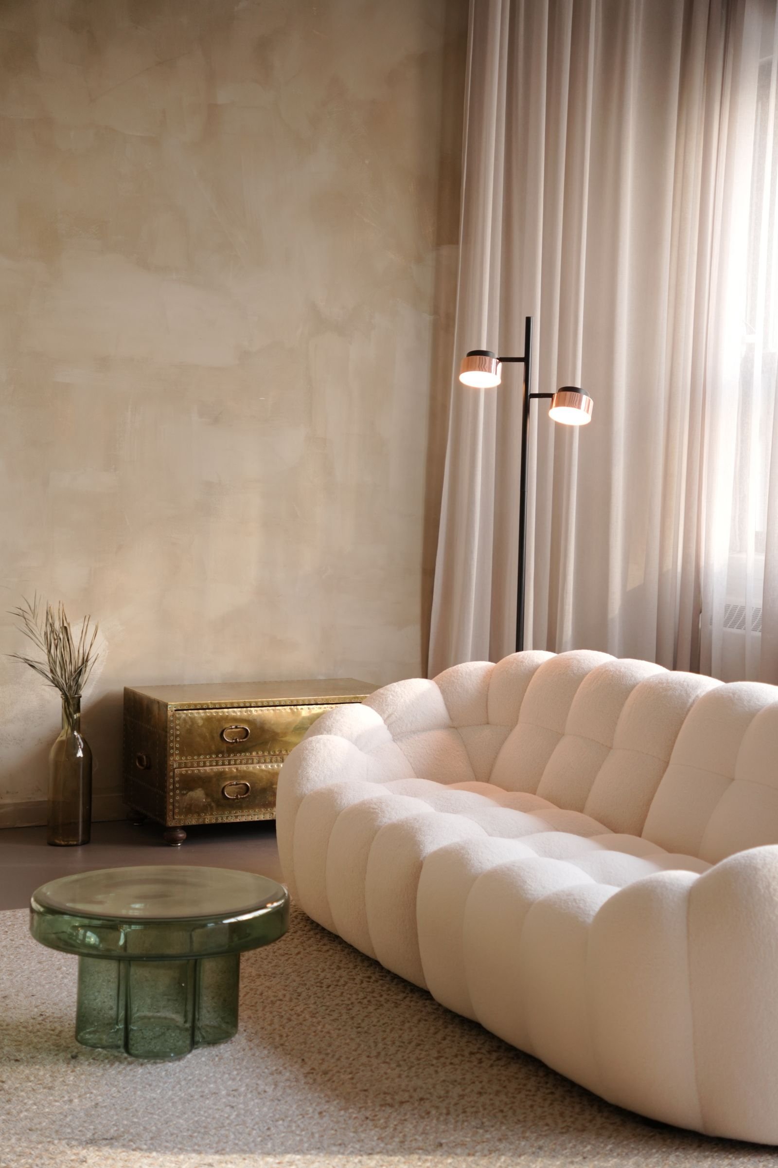 A calm Japandi living room with a cream cloud sofa, textured plaster wall, sheer curtains and a slim floor lamp