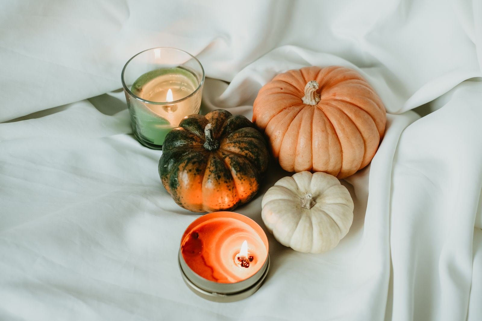 Pumpkins in orange, green and cream with lit candles on a soft white linen
