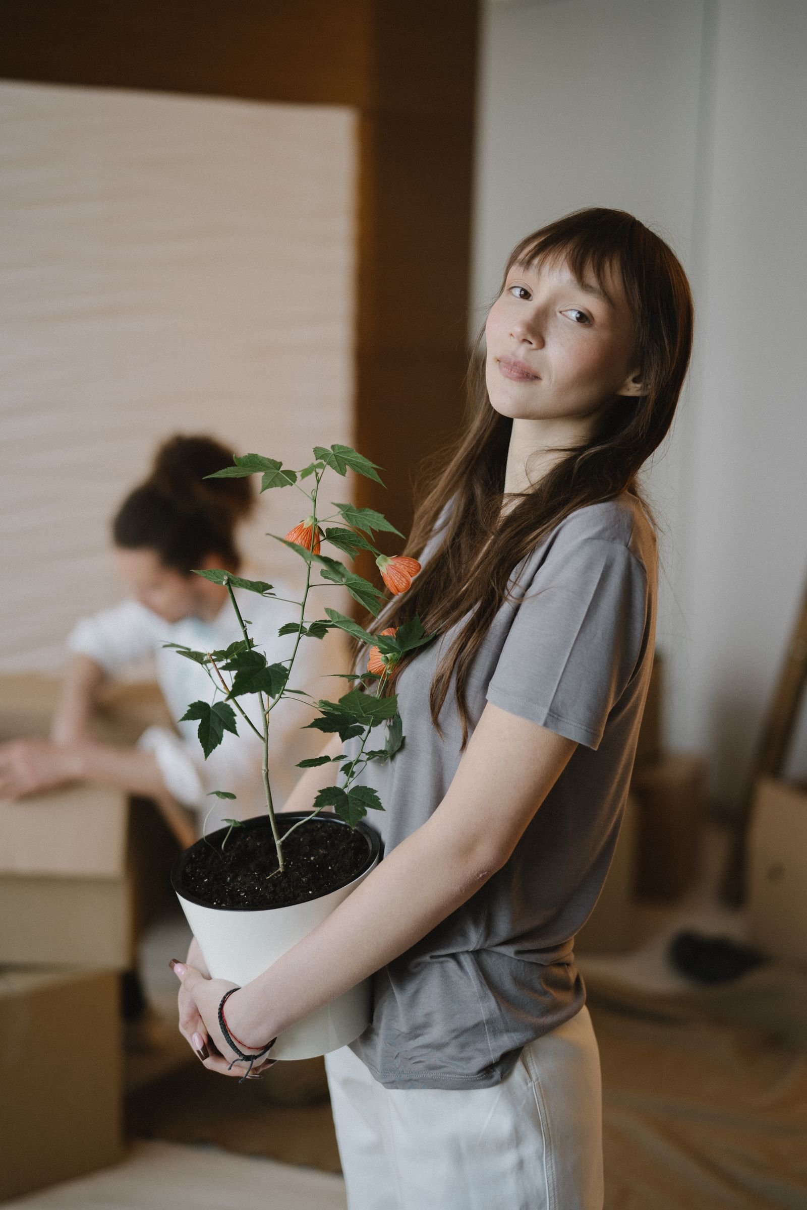 A woman holding a potted plant among moving boxes in a new home