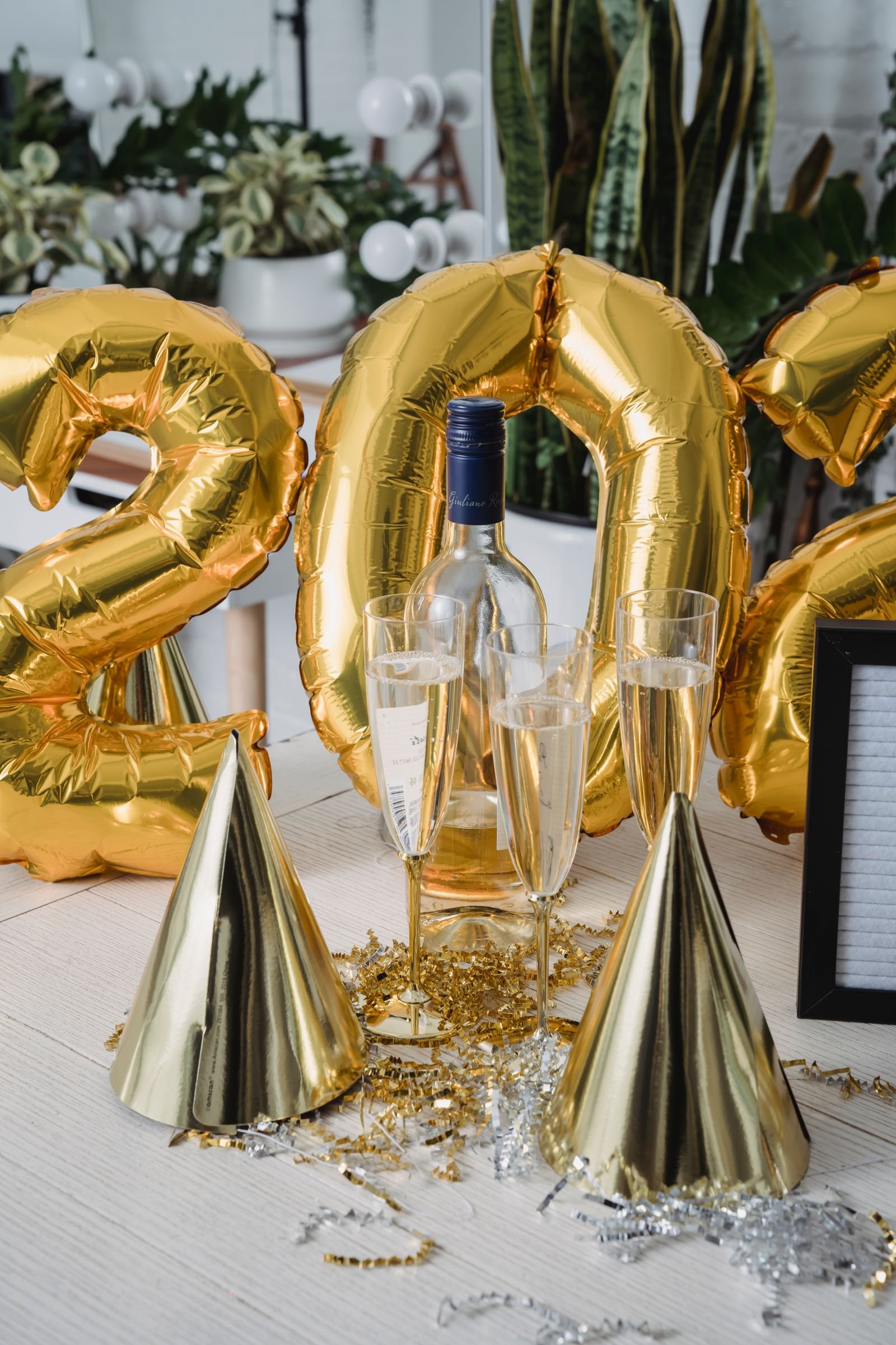 Gold number balloons, gold party hats, champagne flutes and gold confetti on a white party table