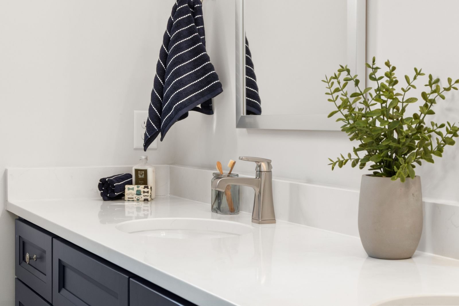A bright white bathroom vanity with a potted plant and a navy striped hand towel