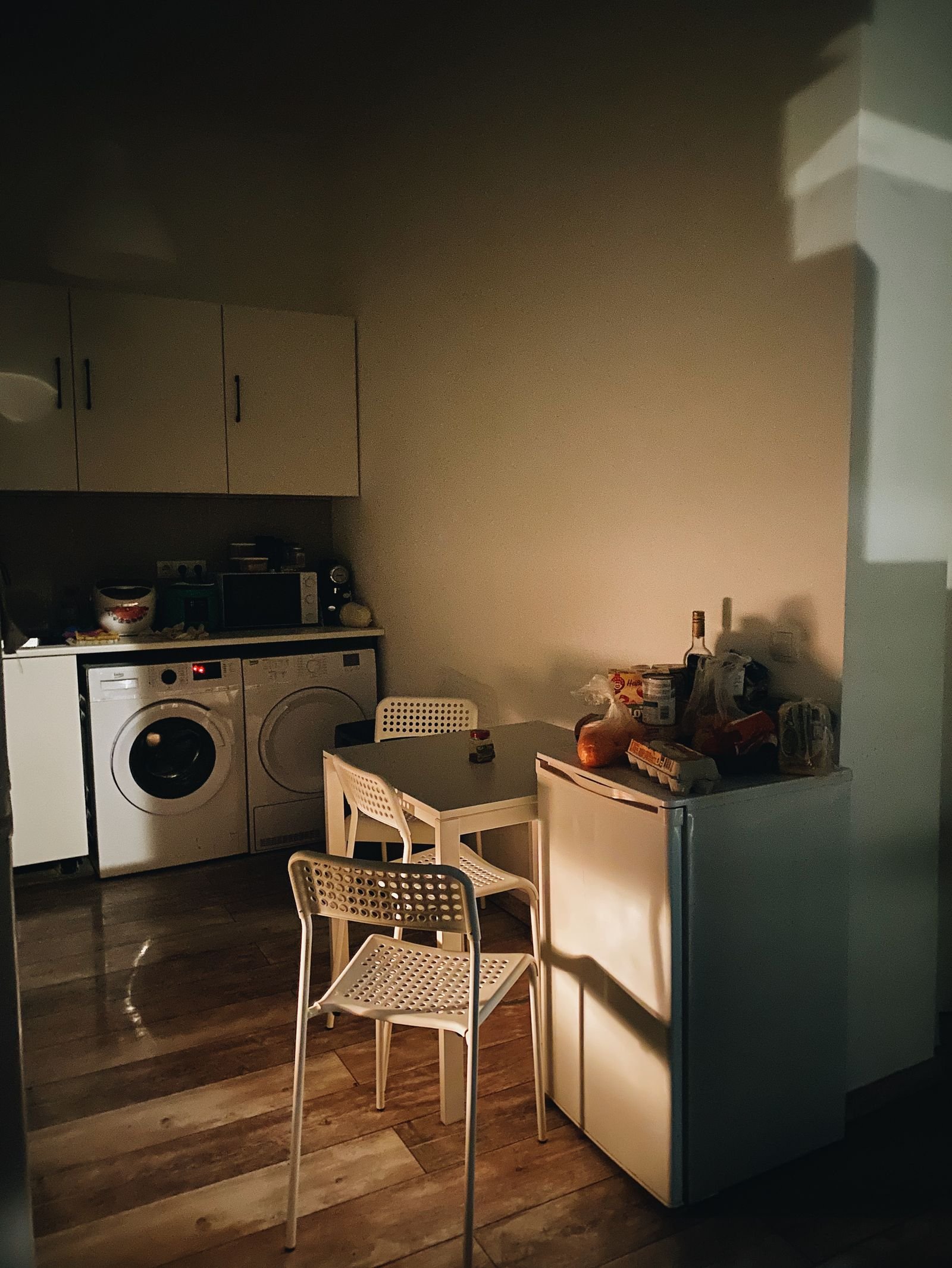 A small apartment kitchen in warm sunlight with compact cabinets, a small table and chairs