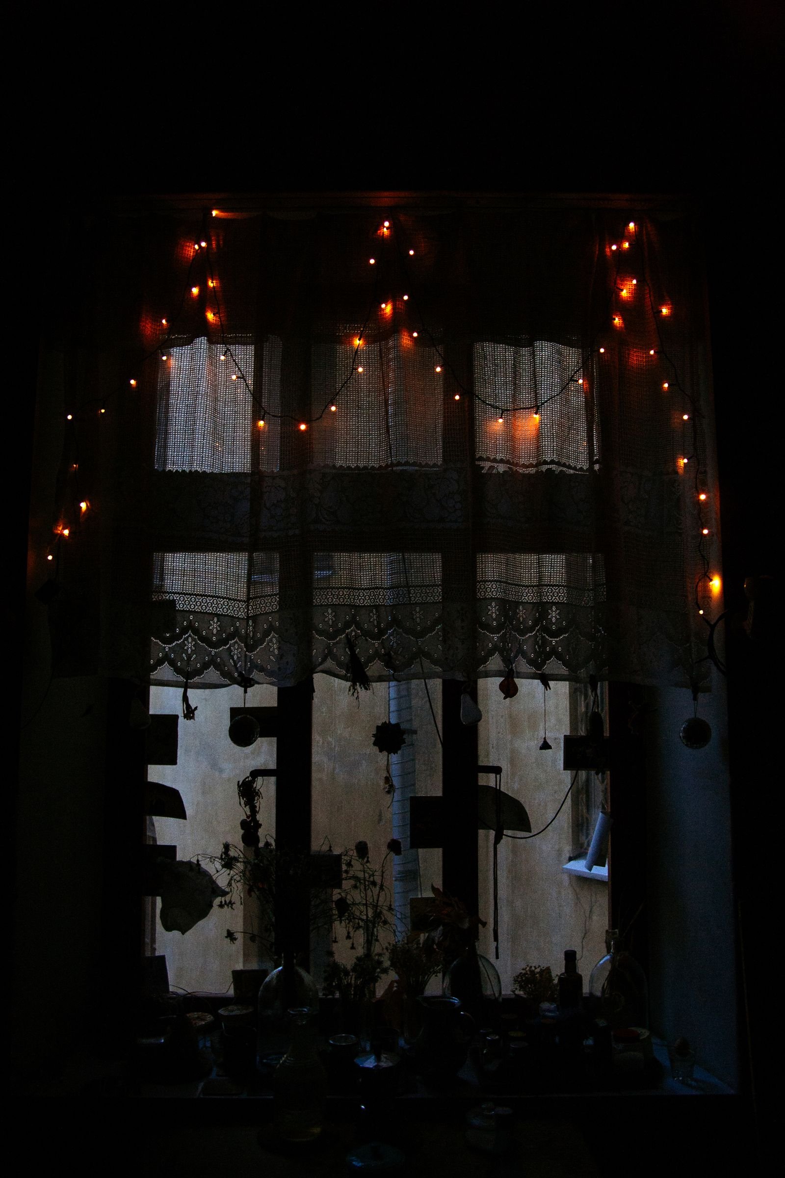 Warm string lights hanging across a lace-curtained window at night