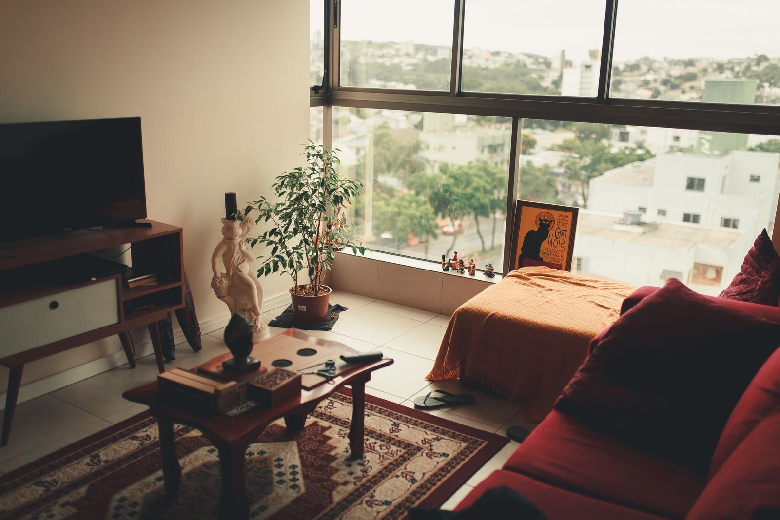 A small studio apartment with a couch, bed, TV console and a rug in front of a large window