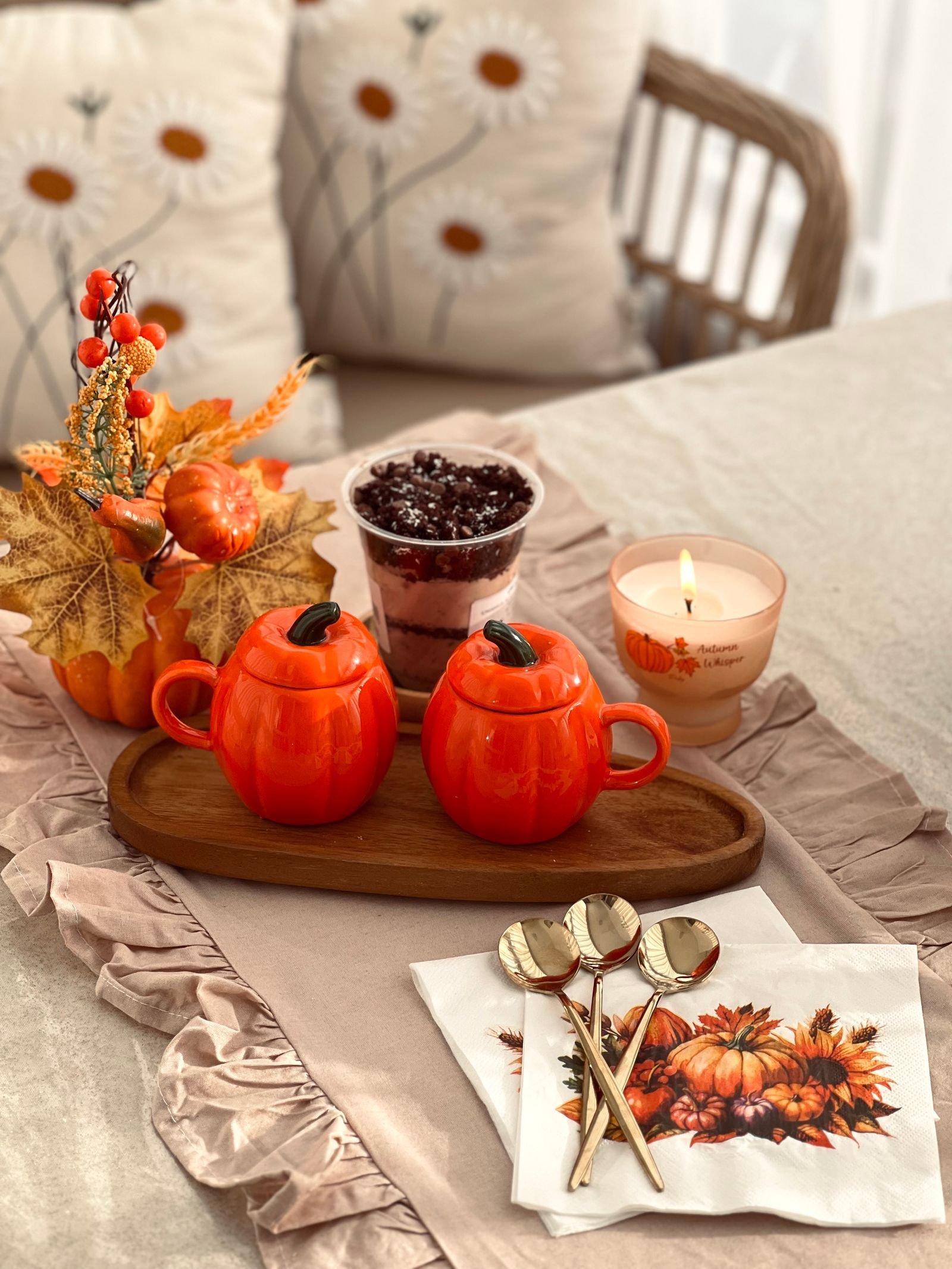 A tray with two orange pumpkin-shaped mugs, a lit candle, small pumpkins and fall leaves on a ruffled table runner